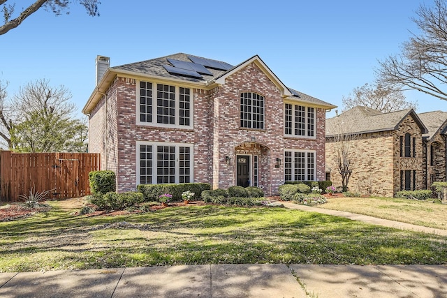 view of front of home with brick siding, solar panels, a front lawn, and fence