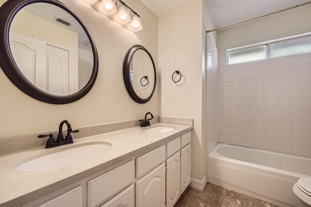 full bath with a textured ceiling, double vanity, visible vents, and a sink