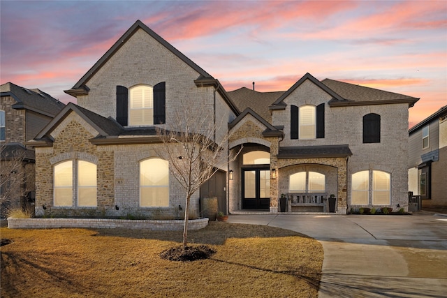 french provincial home featuring brick siding, roof with shingles, and concrete driveway