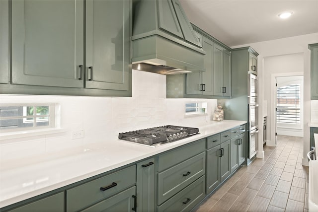 kitchen with green cabinets, premium range hood, stainless steel gas cooktop, light countertops, and decorative backsplash