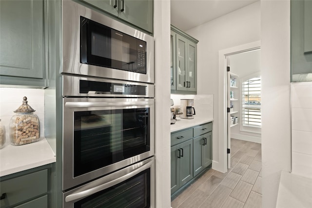 kitchen with backsplash, appliances with stainless steel finishes, light countertops, and green cabinetry