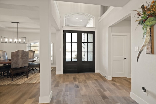 foyer entrance featuring a chandelier, baseboards, wood finished floors, and french doors