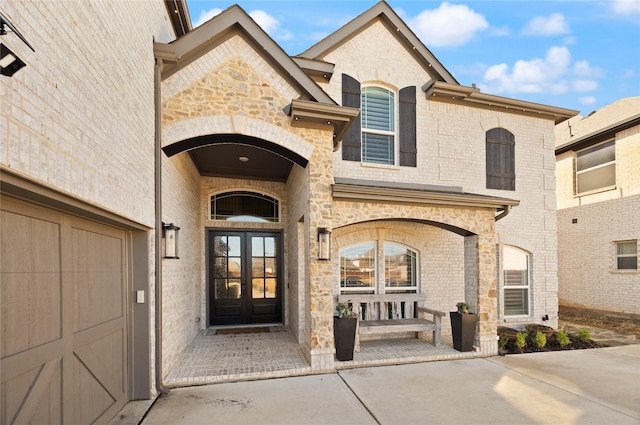 view of exterior entry featuring french doors, stone siding, and brick siding