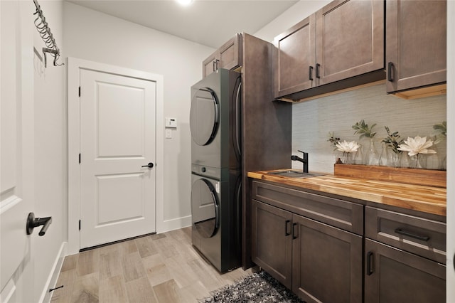 washroom with baseboards, light wood finished floors, cabinet space, a sink, and stacked washer and dryer