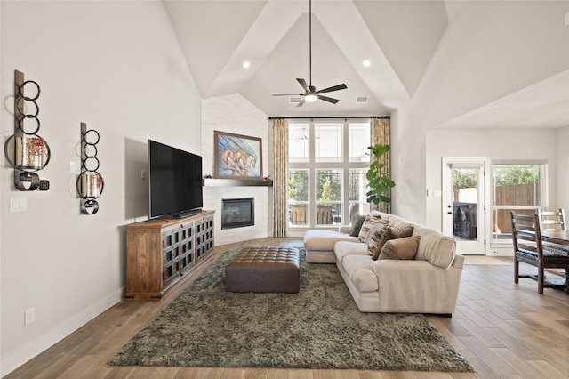 living room with wood finished floors, baseboards, high vaulted ceiling, a fireplace, and recessed lighting