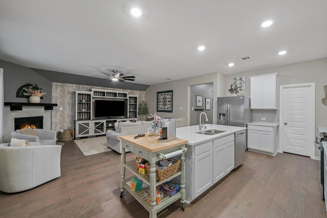 kitchen featuring a stone fireplace, stainless steel appliances, dark wood-style floors, white cabinetry, and a sink