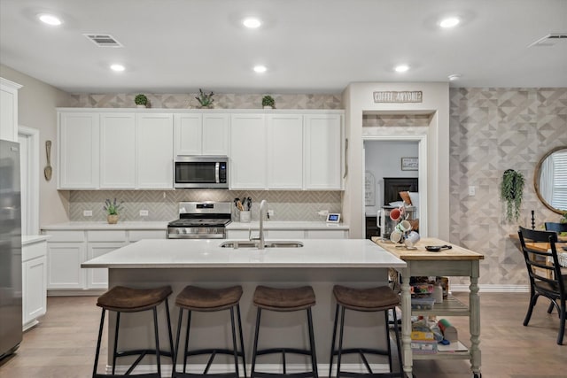 kitchen with a sink, a kitchen bar, appliances with stainless steel finishes, and white cabinets