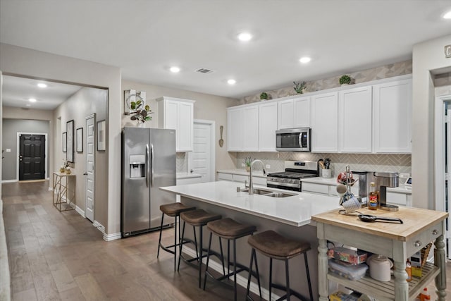 kitchen featuring a center island with sink, a sink, white cabinetry, appliances with stainless steel finishes, and light countertops