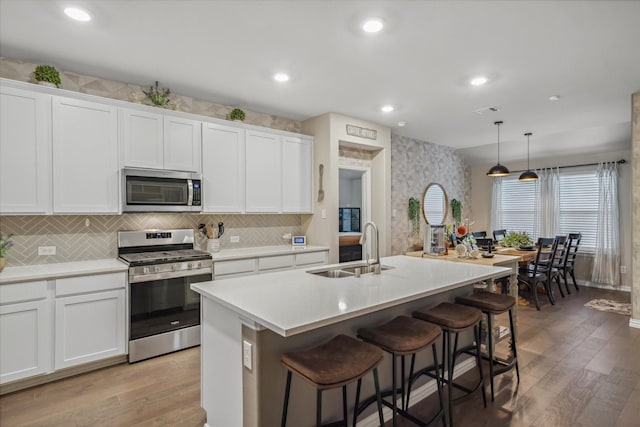 kitchen with light wood finished floors, stainless steel appliances, an island with sink, and a sink