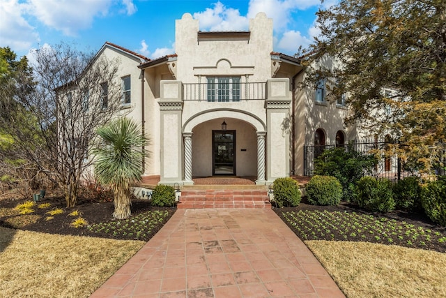 view of exterior entry with a balcony, fence, a porch, stucco siding, and a tiled roof