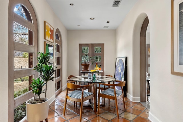 dining area with light tile patterned floors, arched walkways, visible vents, and baseboards