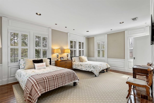 bedroom with visible vents, crown molding, recessed lighting, wood finished floors, and a decorative wall