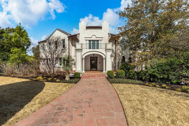 mediterranean / spanish-style house featuring stucco siding, a balcony, a front yard, and a tiled roof