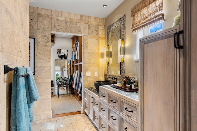 full bath featuring stone tile flooring, tile walls, and vanity