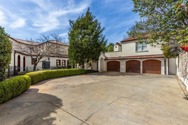 mediterranean / spanish house featuring fence, a tiled roof, stucco siding, a garage, and driveway