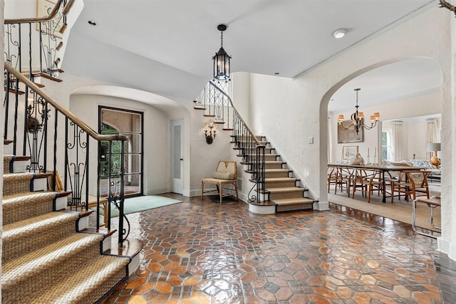 entrance foyer featuring baseboards, arched walkways, stairs, stone finish floor, and a chandelier