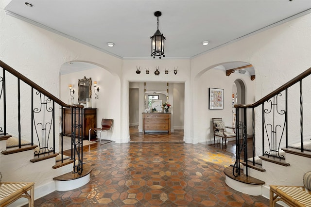 entrance foyer with arched walkways, stairway, a textured wall, and ornamental molding