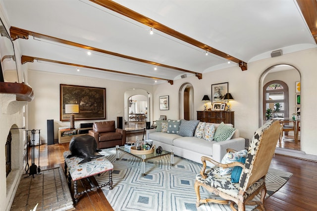 living room featuring visible vents, beam ceiling, a fireplace with raised hearth, hardwood / wood-style flooring, and arched walkways