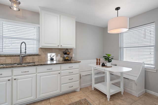 kitchen featuring decorative backsplash, dark stone counters, white cabinetry, and a sink