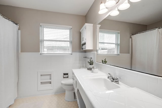 bathroom featuring vanity, a wainscoted wall, tile patterned flooring, tile walls, and toilet