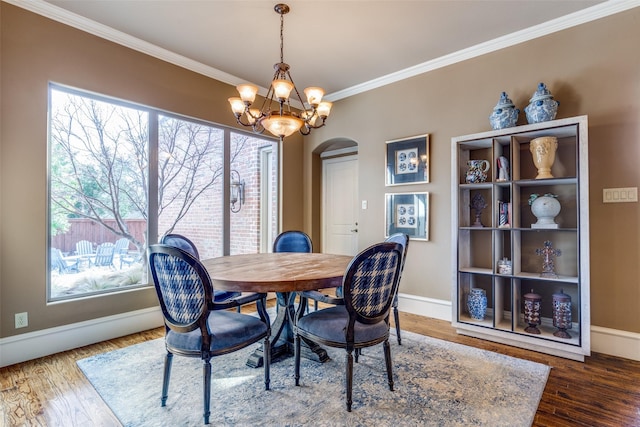 dining space featuring a chandelier, arched walkways, wood finished floors, and crown molding