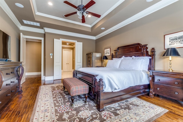 bedroom with wood finished floors, baseboards, visible vents, a tray ceiling, and ornamental molding