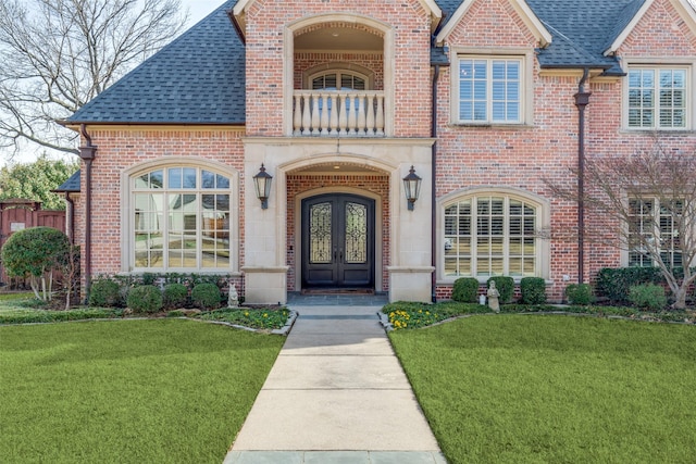 doorway to property with a balcony, a yard, french doors, and brick siding