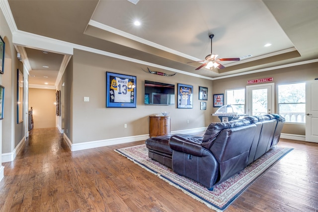 living area with crown molding, a raised ceiling, and wood finished floors