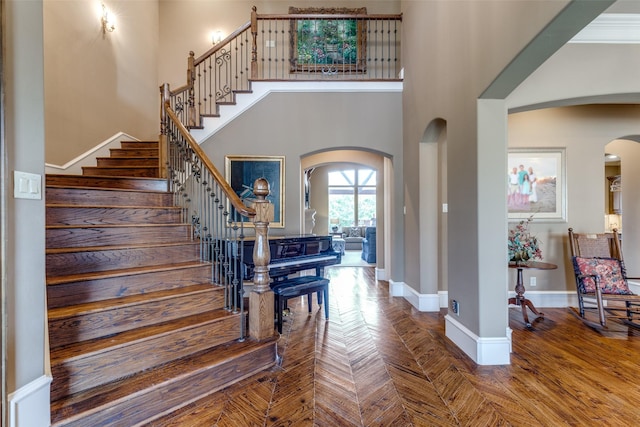 entryway with baseboards, arched walkways, a towering ceiling, and stairs