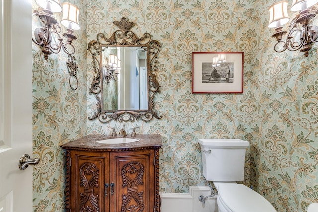 bathroom with toilet, vanity, and wallpapered walls