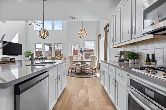 kitchen with visible vents, light wood-type flooring, decorative backsplash, appliances with stainless steel finishes, and a sink