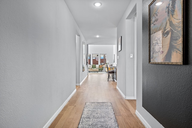 hallway featuring light wood-style floors, baseboards, and a textured wall