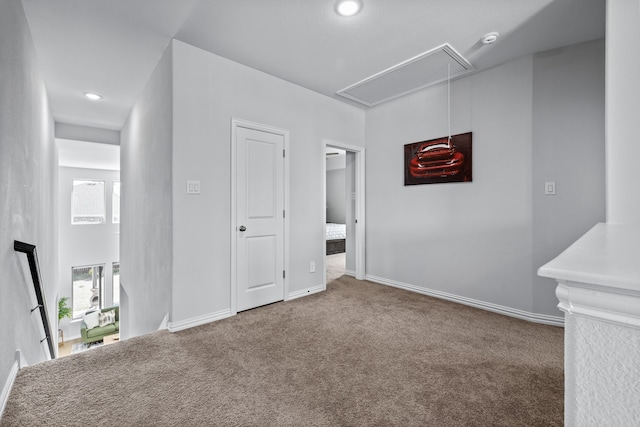 carpeted empty room with attic access and baseboards