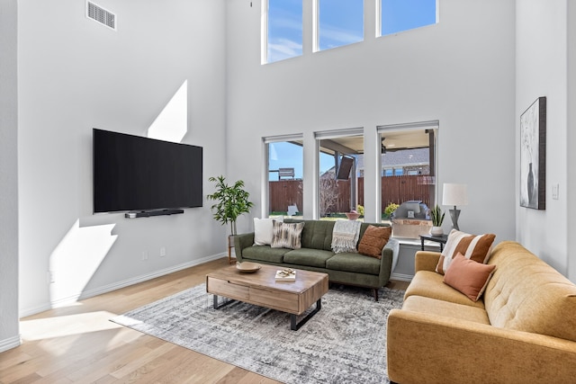 living room featuring a high ceiling, wood finished floors, visible vents, and baseboards