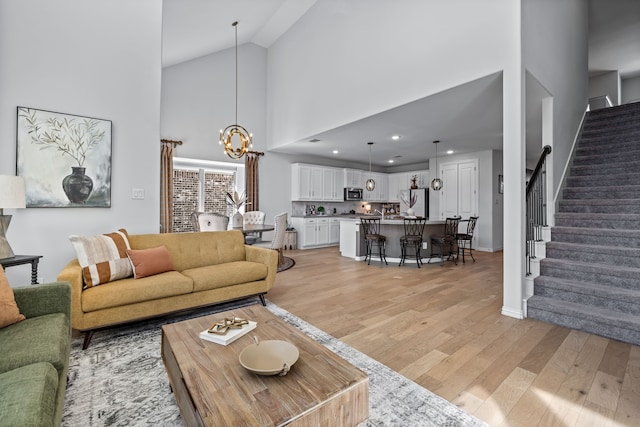 living area with high vaulted ceiling, recessed lighting, stairway, light wood finished floors, and a chandelier