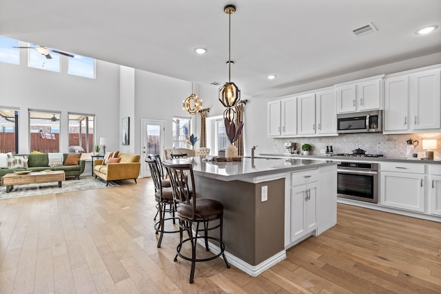 kitchen with tasteful backsplash, visible vents, an island with sink, a kitchen breakfast bar, and stainless steel appliances