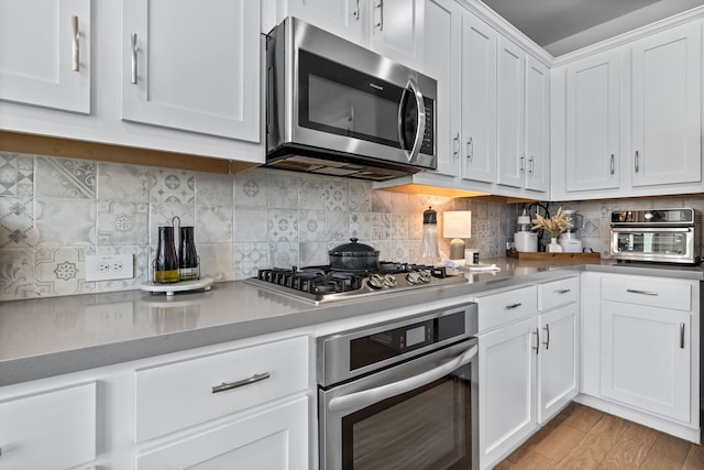 kitchen with light wood finished floors, a toaster, stainless steel appliances, white cabinetry, and backsplash