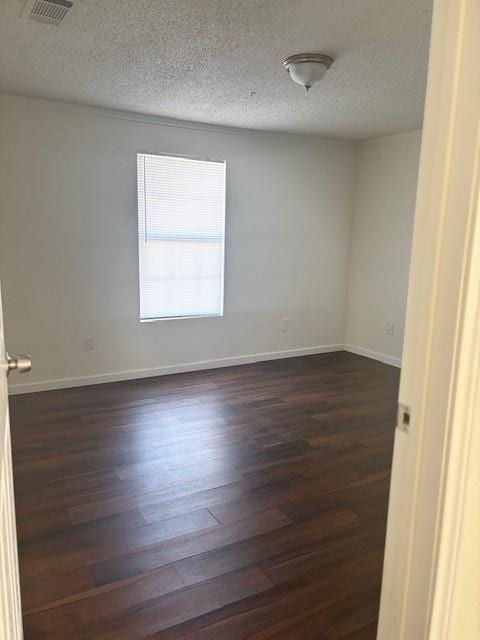 spare room with dark wood-type flooring, visible vents, baseboards, and a textured ceiling