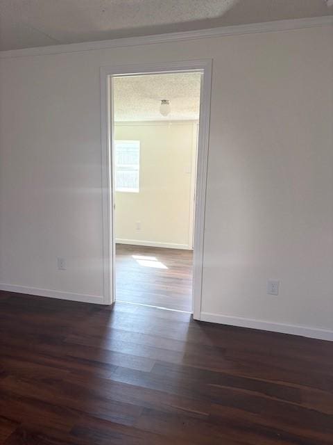 spare room with baseboards, dark wood-type flooring, crown molding, and a textured ceiling