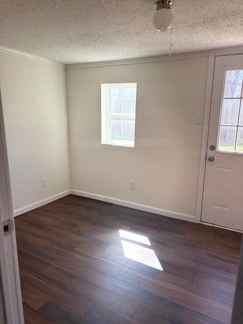 empty room with dark wood finished floors, a textured ceiling, and baseboards