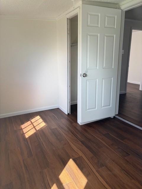 unfurnished bedroom with baseboards, a textured ceiling, ornamental molding, and dark wood-style flooring