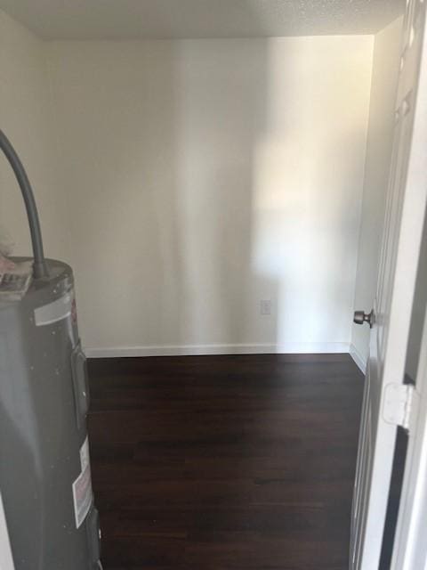 unfurnished room featuring baseboards, dark wood-type flooring, water heater, and a textured ceiling