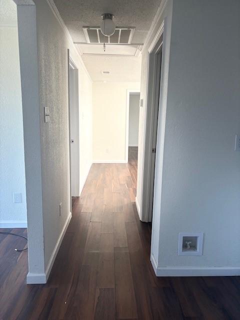 hall with visible vents, baseboards, attic access, and dark wood-style floors