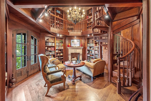 living area featuring wood finished floors, french doors, stairway, a lit fireplace, and wooden walls