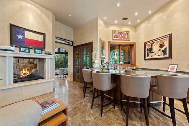 bar with stone tile floors, visible vents, recessed lighting, a multi sided fireplace, and a towering ceiling