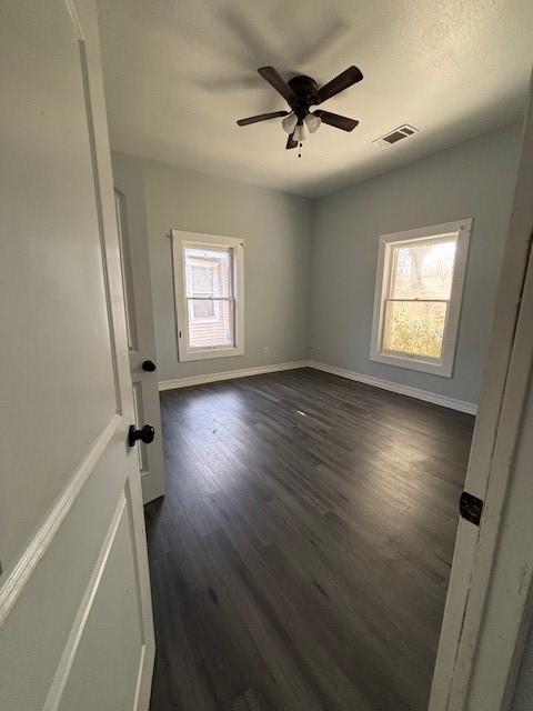 unfurnished bedroom with multiple windows, dark wood-style floors, visible vents, and baseboards