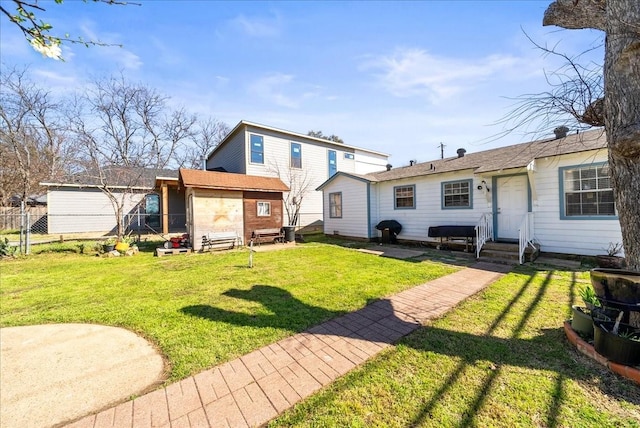 rear view of house with entry steps, an outdoor structure, a yard, and fence