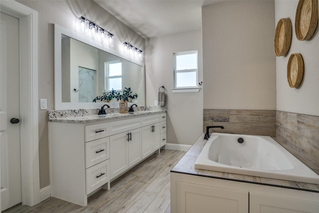 bathroom featuring a garden tub, wood finished floors, double vanity, and a sink