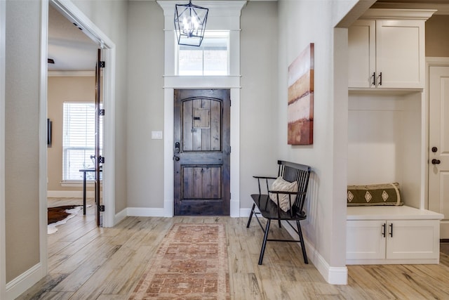 foyer entrance featuring ornamental molding, light wood-style floors, baseboards, and a chandelier