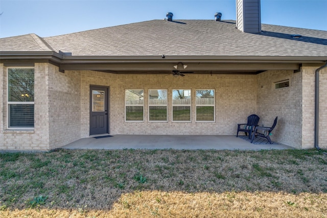 exterior space featuring a lawn, a shingled roof, brick siding, ceiling fan, and a patio area